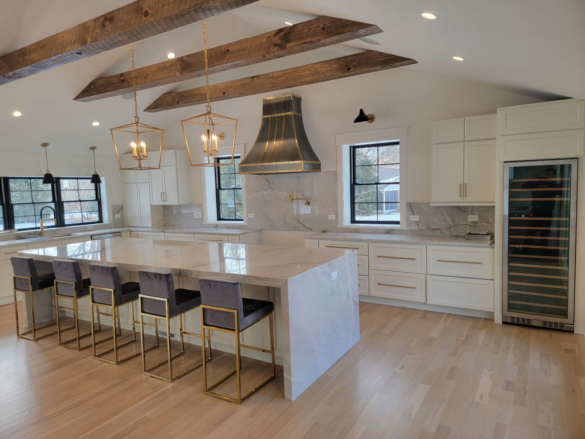 Modern kitchen with white cabinets, marble island, wood beams, pendant lights, and bar stools