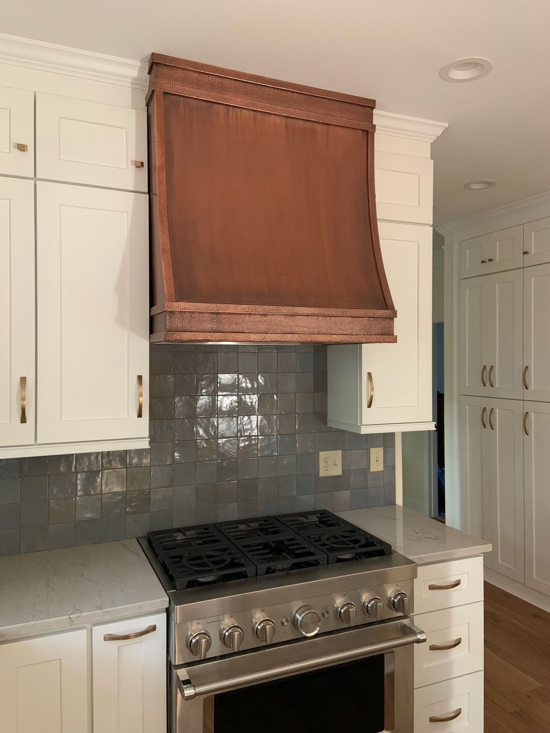 Kitchen stove with stainless steel range, gray tile backsplash, white cabinets, and brown wood hood cover