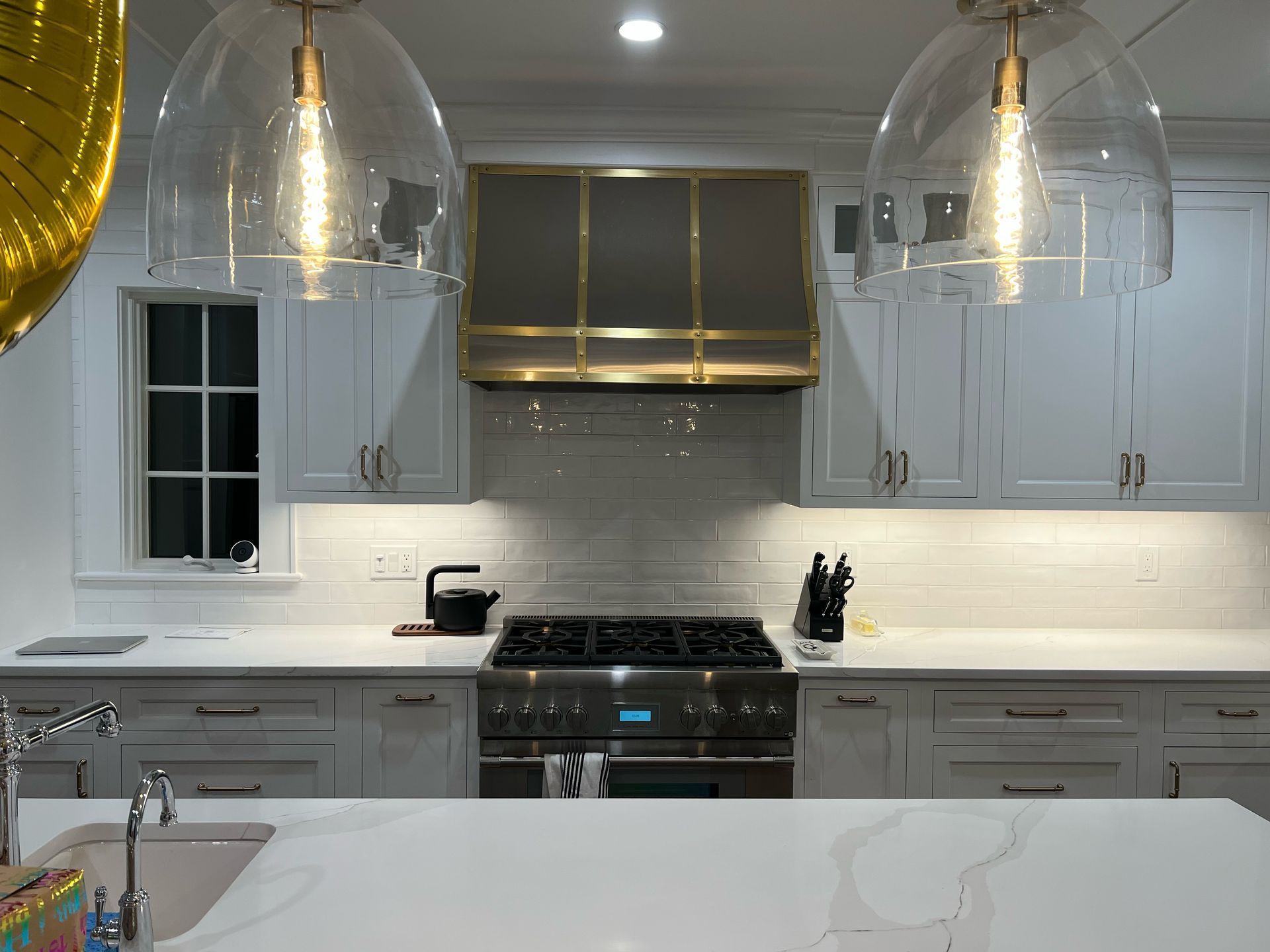 Bright modern kitchen with white cabinets, marble counters, gold pendant lights, and a stainless stove