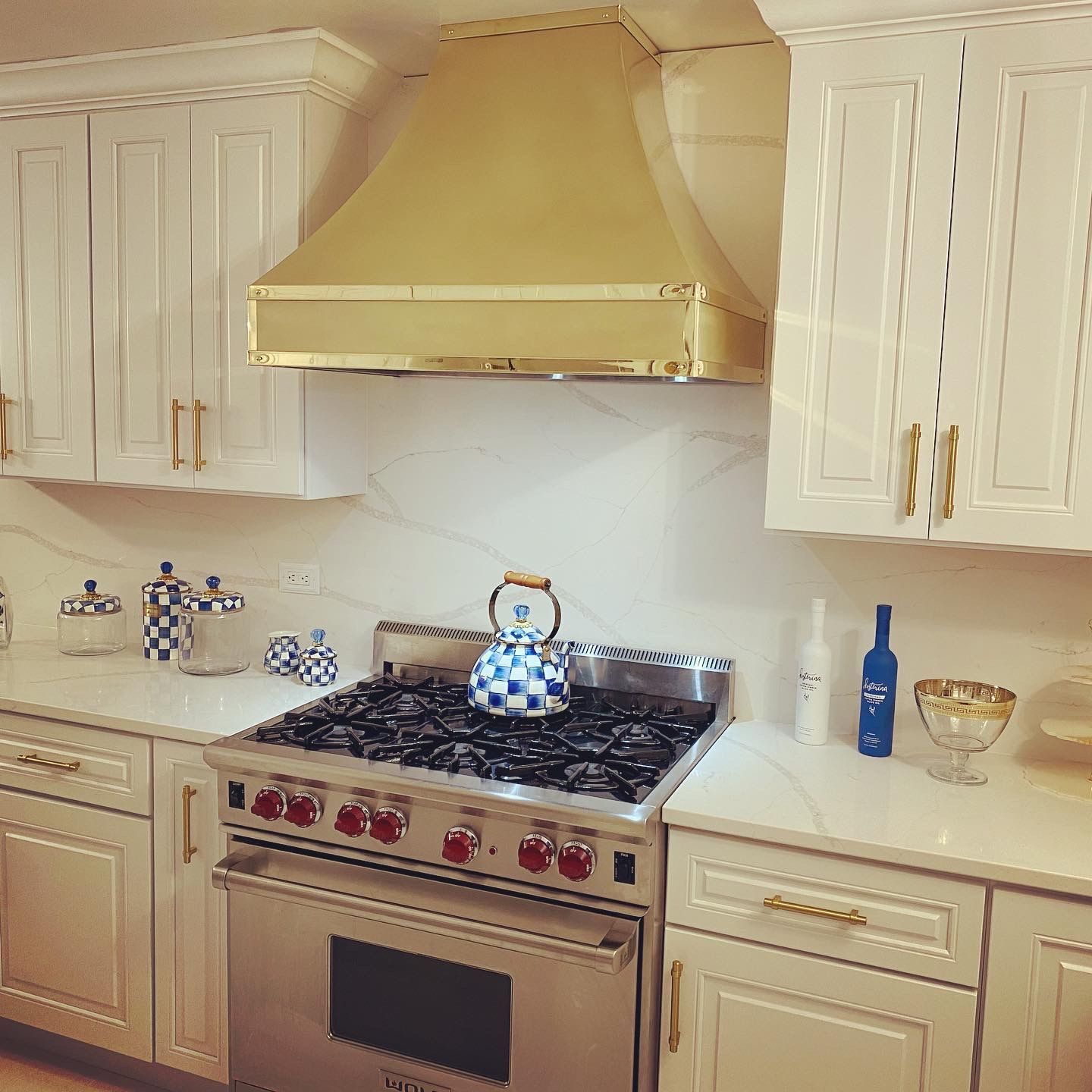 White kitchen with gold range hood, stainless stove, and blue-and-white decor on the counters