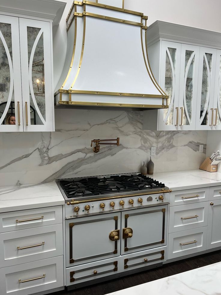 Elegant white kitchen with gold accents, marble backsplash, and a stainless steel range with hood