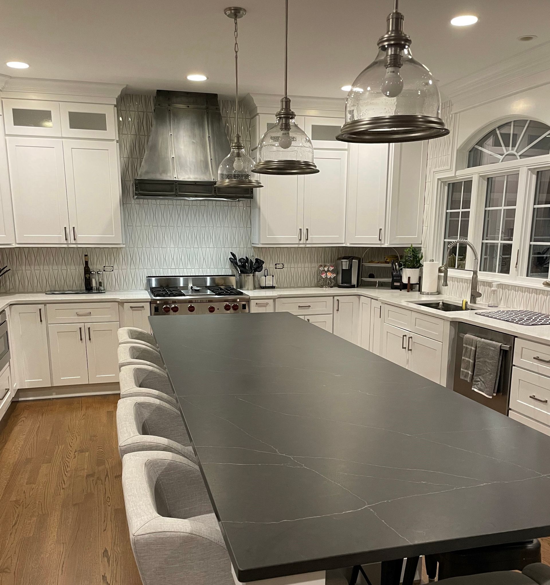 Modern kitchen with a long dark island, white cabinets, pendant lights, and hardwood floor