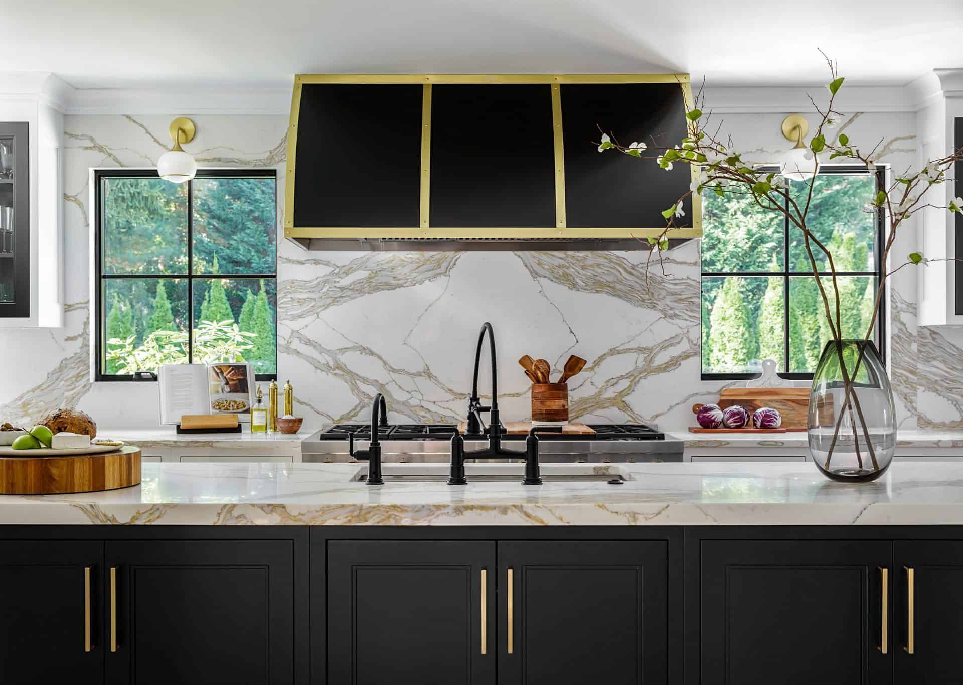 Modern kitchen with black cabinets, gold accents, marble backsplash, and a large window above the sink