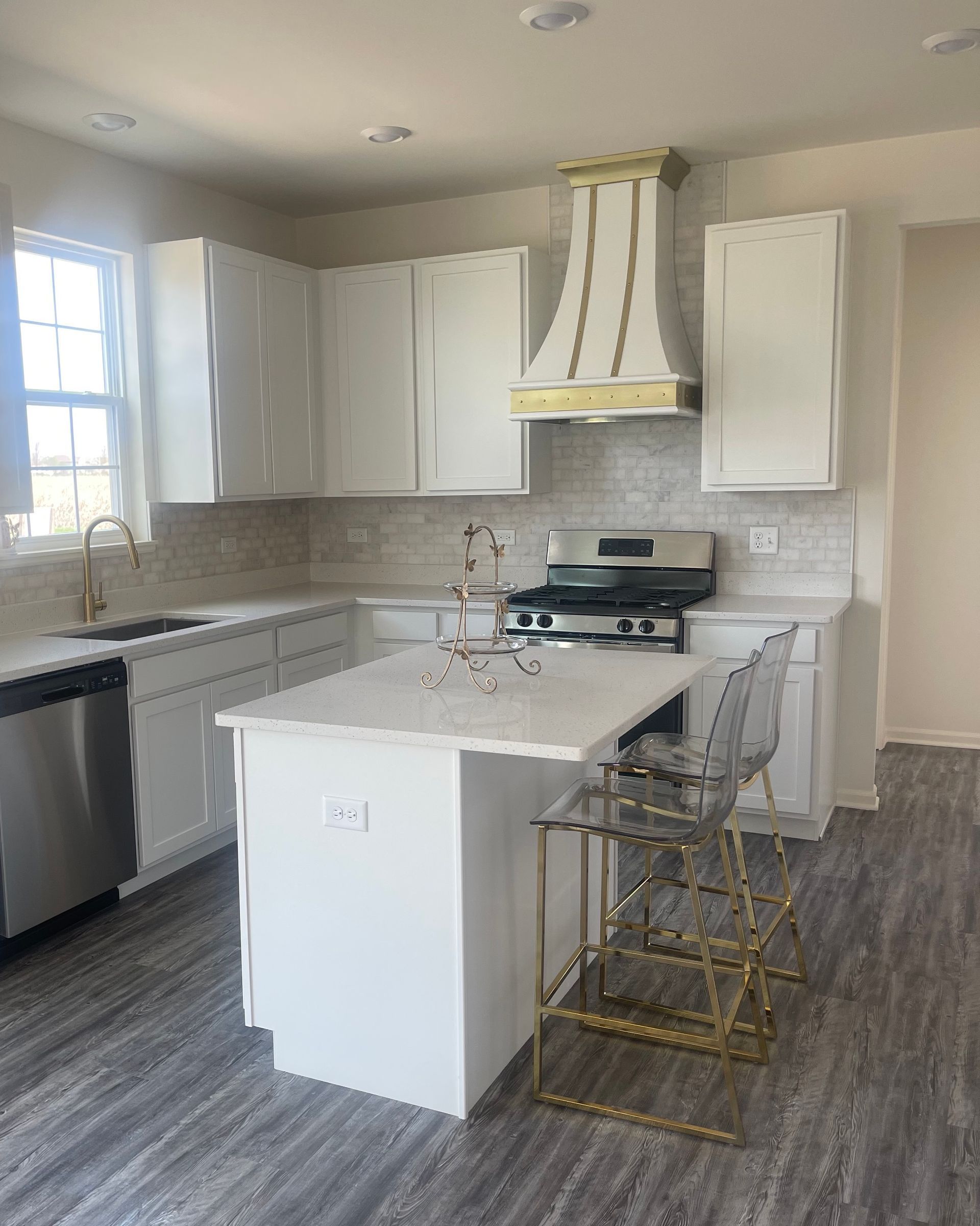 Bright modern kitchen with white cabinets, island, stainless appliances, and gray wood flooring