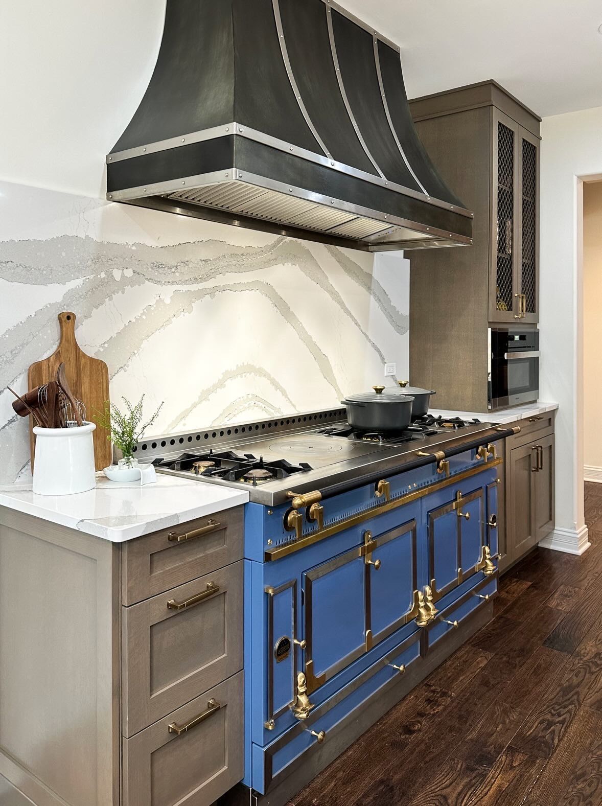 Modern kitchen with blue range cabinets, marble backsplash, dark countertops, and stainless steel hood and stove.