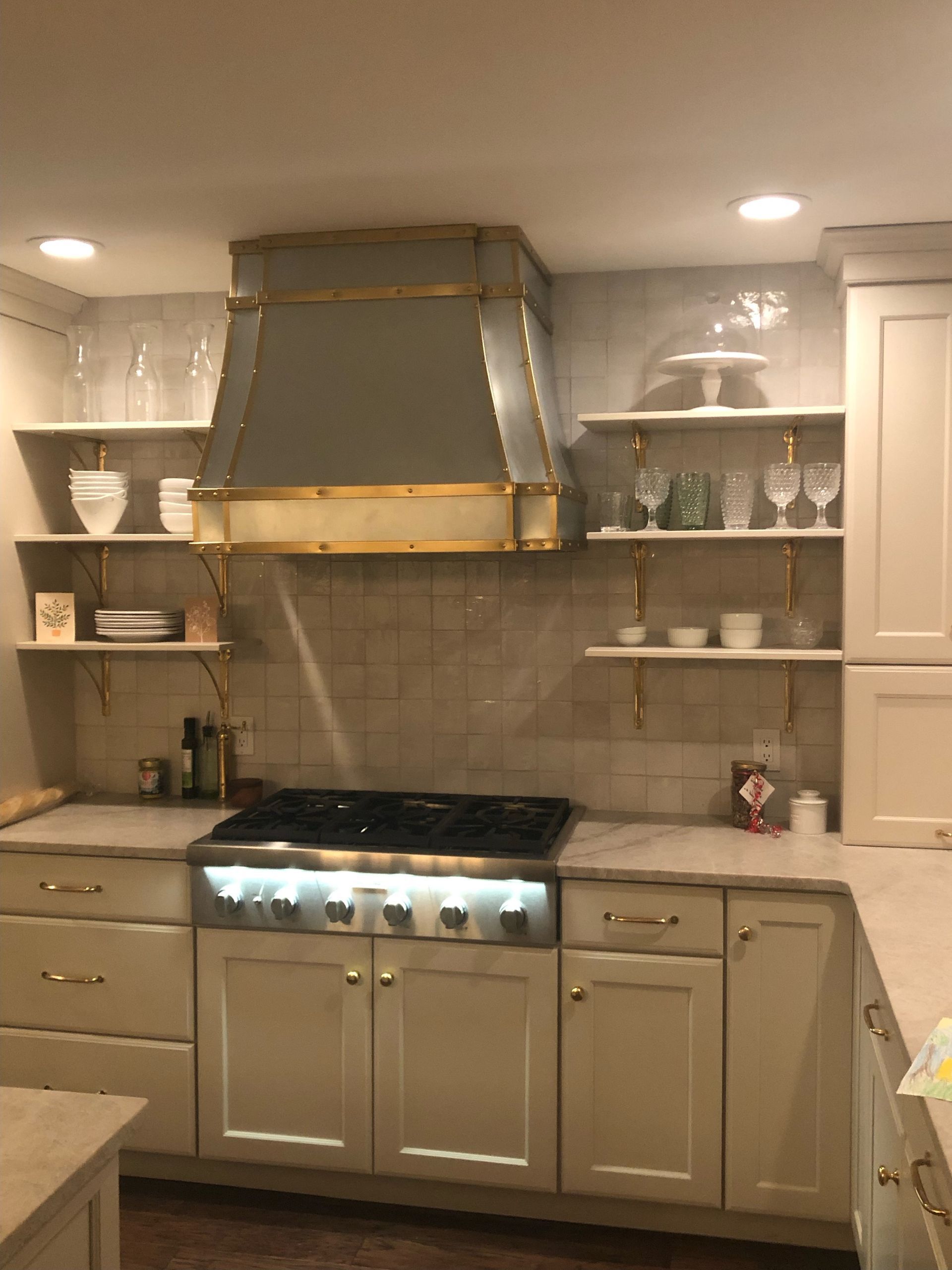 Modern kitchen with beige cabinets, stainless range hood, and white countertops under warm lighting