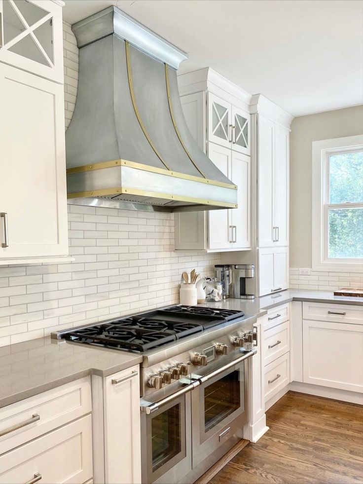Bright white kitchen with gas range, stainless hood, subway tile backsplash, and wood floor