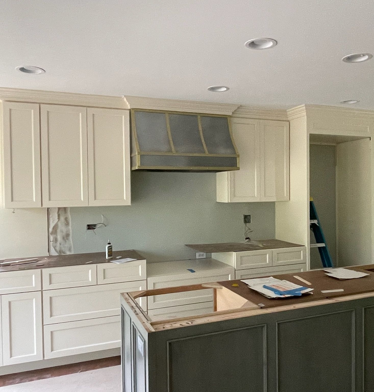 Modern kitchen under renovation with white cabinets, range hood, and island under construction