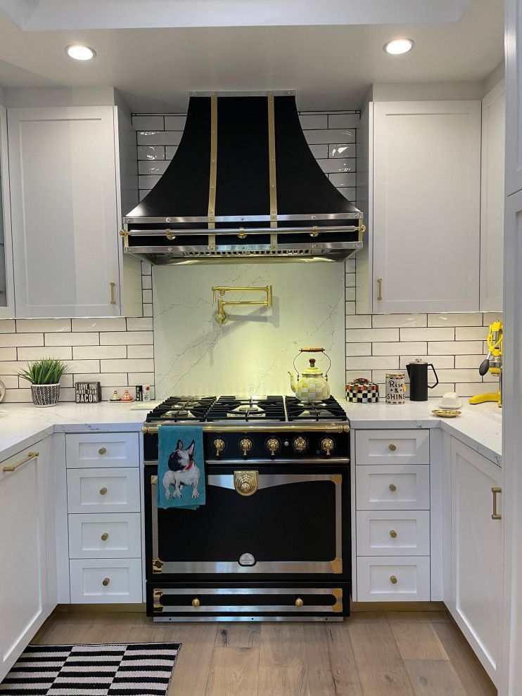 Bright white kitchen with black-and-gold stove and range hood, white cabinets, and marble countertops