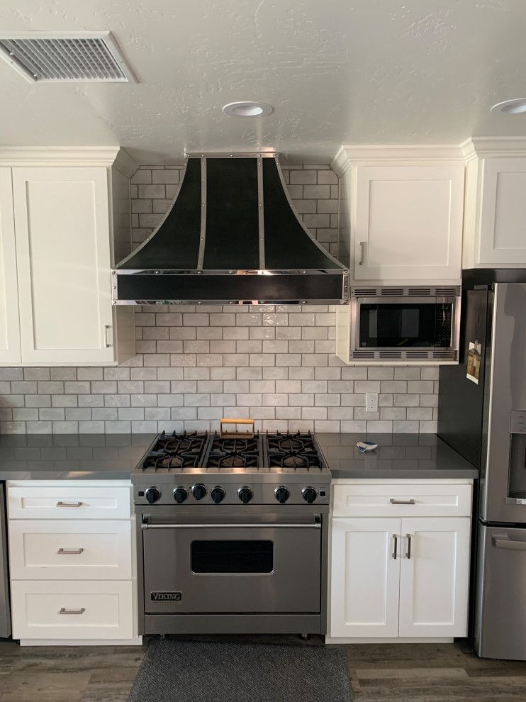 Modern kitchen with white cabinets, gray subway tile backsplash, stainless stove, black range hood, and microwave.