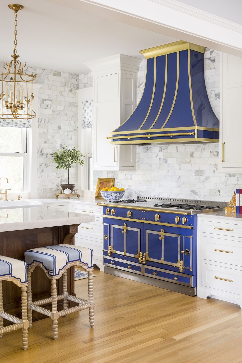 Elegant kitchen with cobalt-blue range hood and stove, white cabinetry, marble backsplash, and gold accents