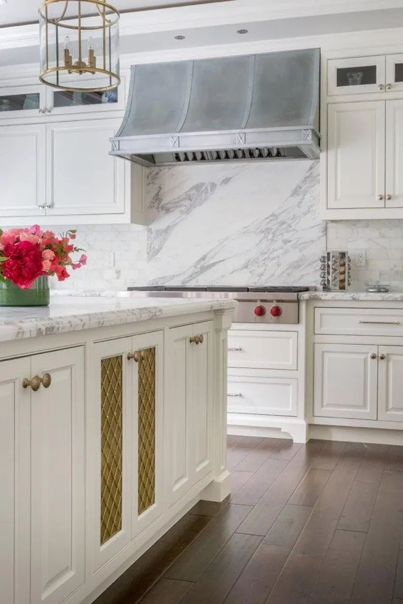 Elegant white kitchen with marble backsplash, gold accents, and a stainless range hood