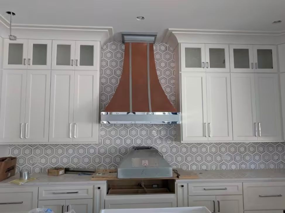 Modern kitchen with white cabinets, patterned backsplash, and copper range hood