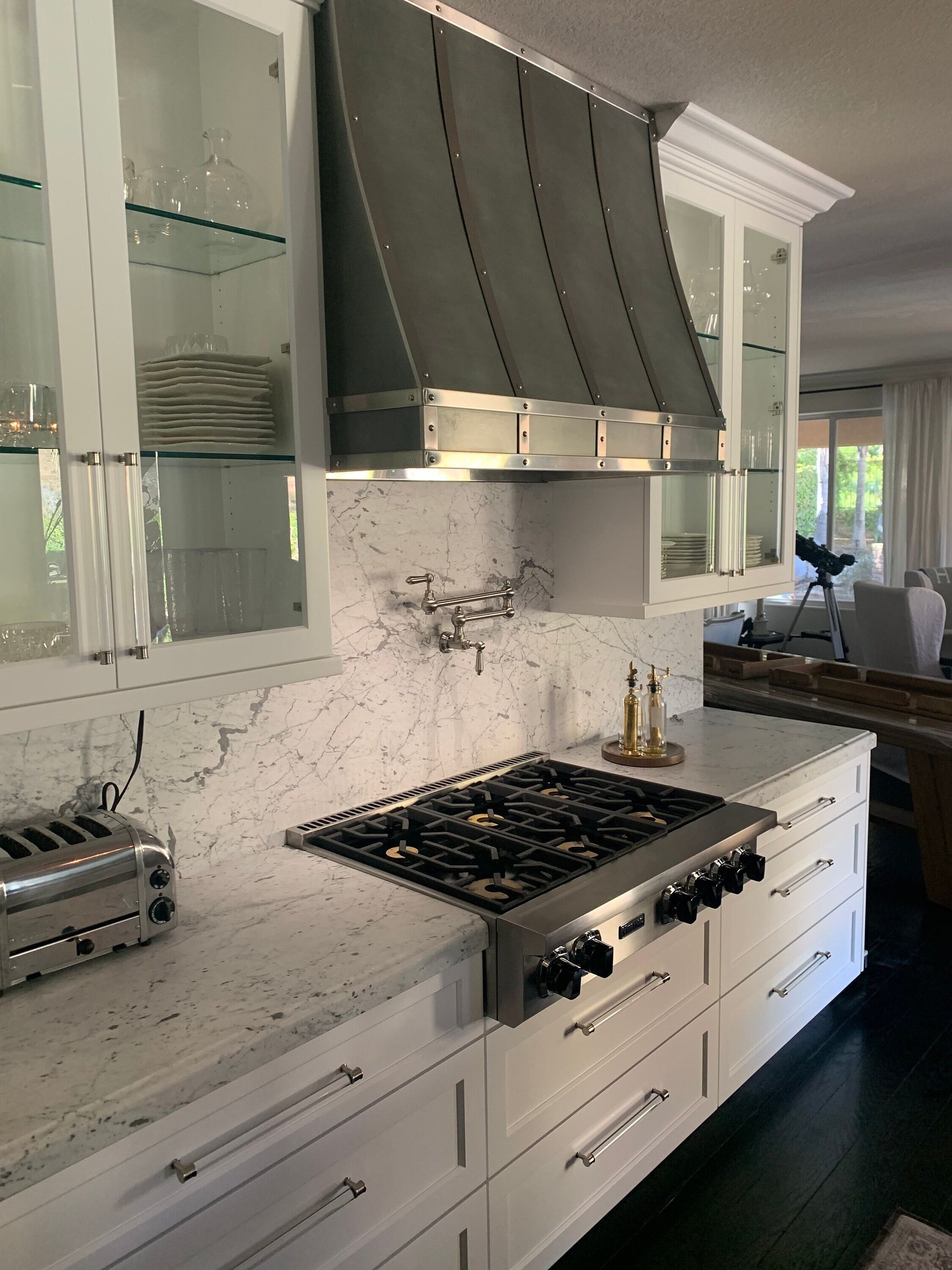 Bright kitchen with white cabinets, marble backsplash, gas range, and dark gray vent hood