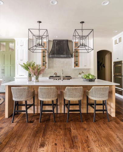 Bright modern kitchen with white island, woven stools, black pendant lights, and hardwood floors