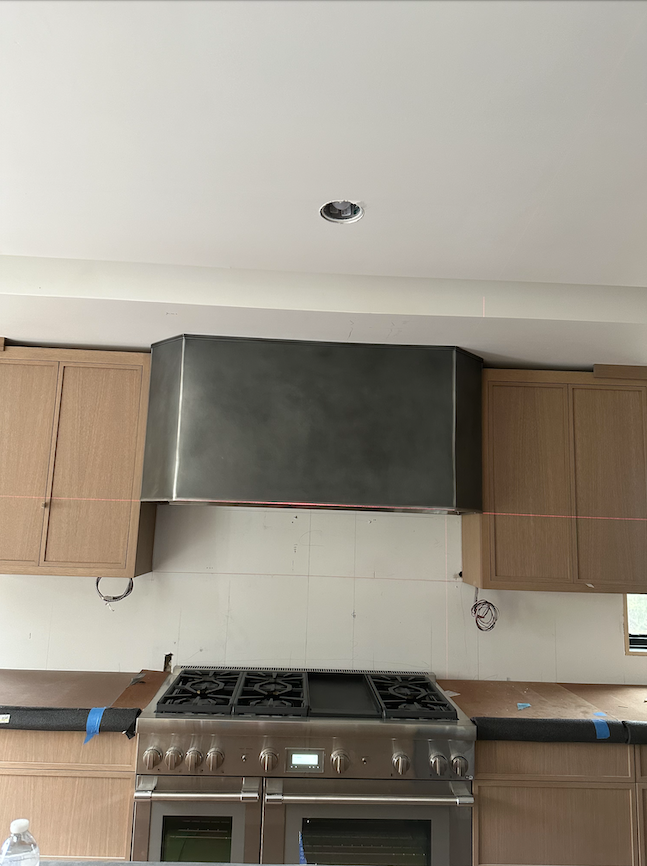 Kitchen with a stainless-steel range hood, gas stove, and light wood cabinets on both sides.