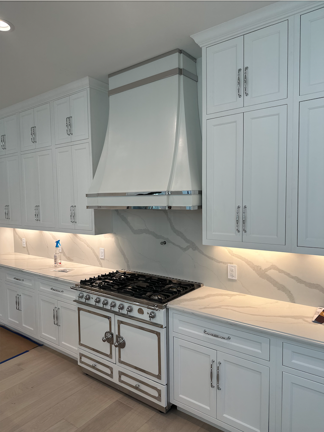 White luxury kitchen with cabinets, marble countertops, and a stainless range hood over a gas stove.