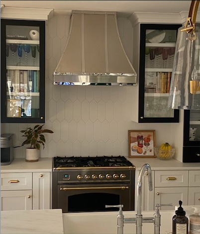 Modern kitchen with white cabinets, stainless range hood, gas stove, and marble countertop with sink.