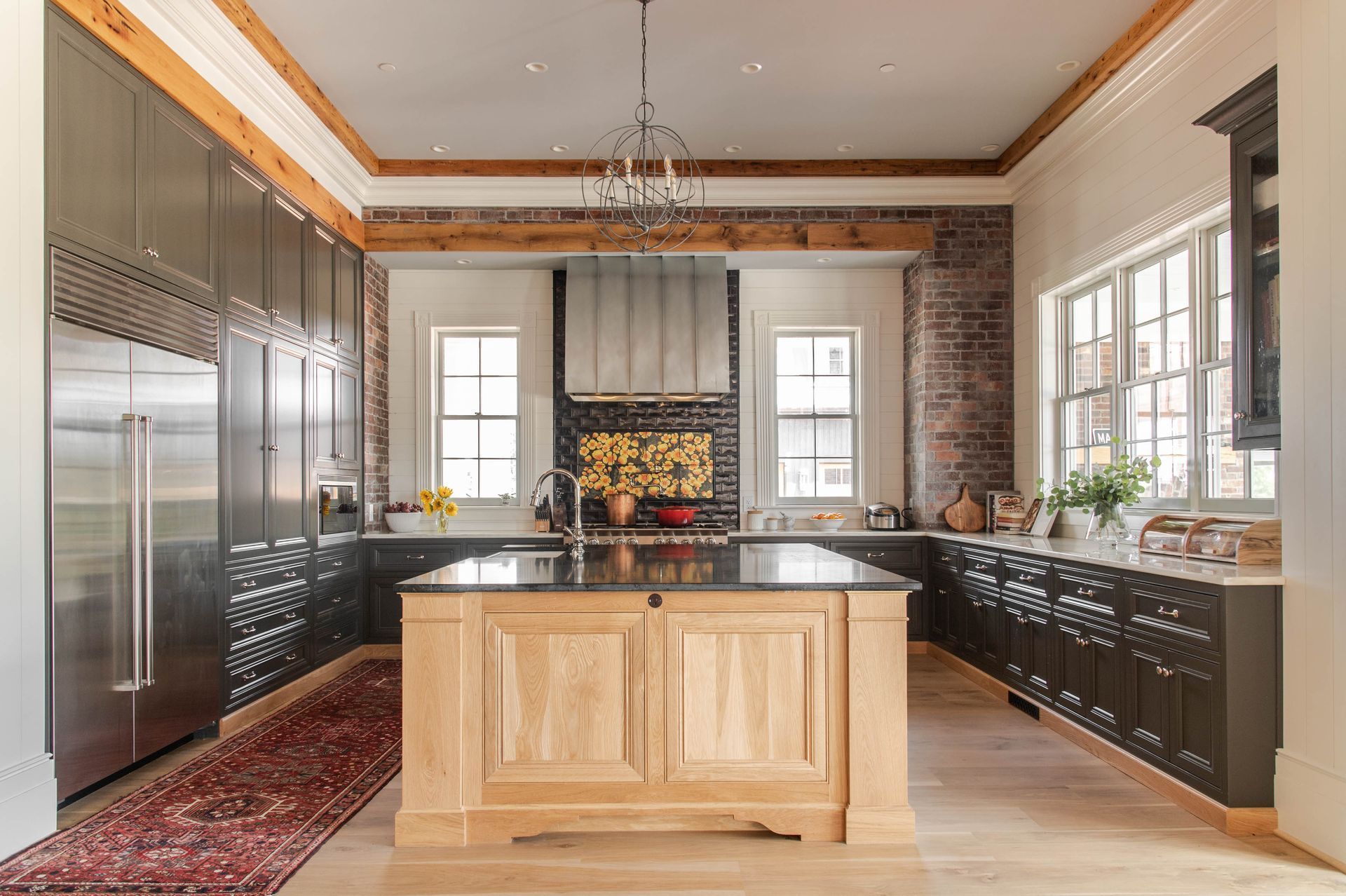 Spacious modern kitchen with light wood island, dark cabinetry, stainless appliances, and large windows