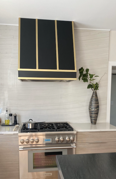 Modern kitchen with stainless steel stove, black-and-gold cabinets, white backsplash, and vase of greenery