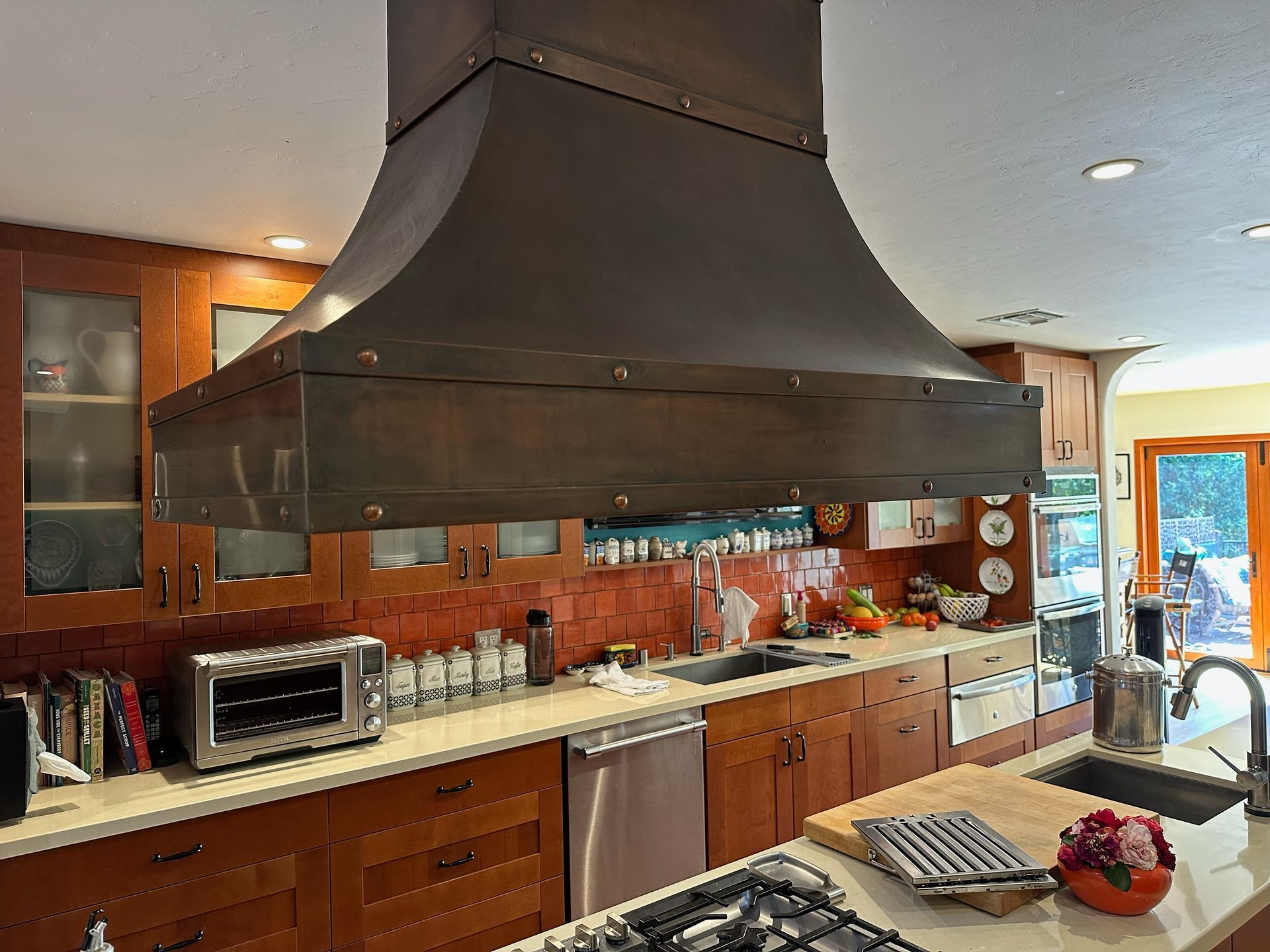 Modern kitchen with a large black range hood, wood cabinets, stainless appliances, and a fruit bowl on the island
