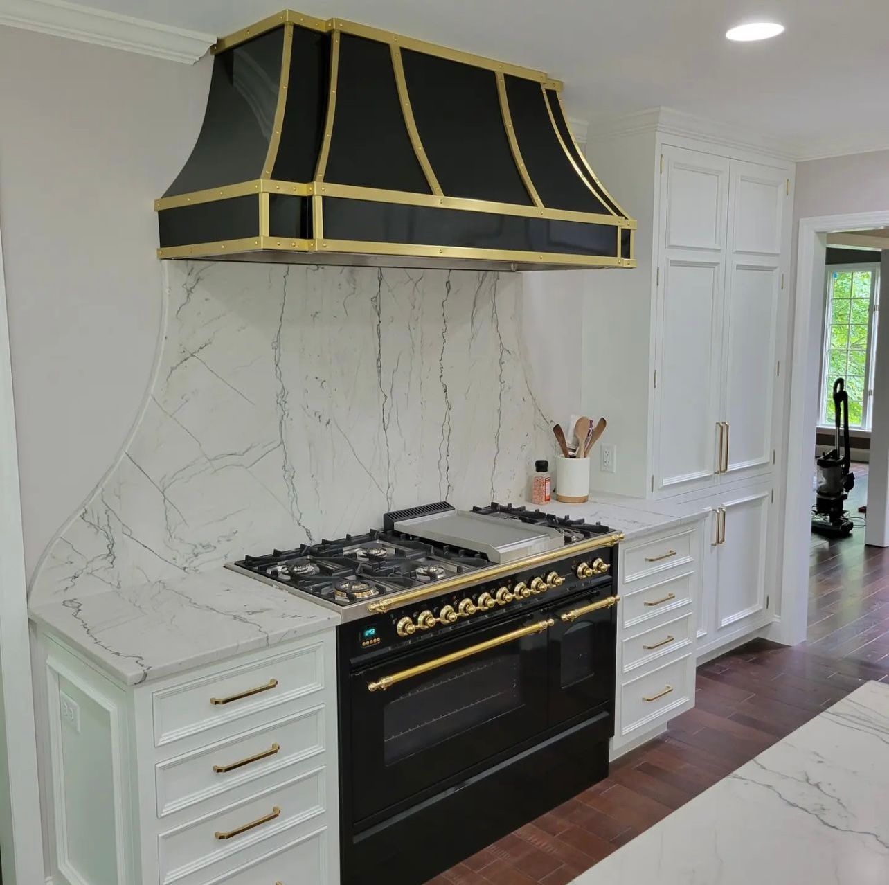 Elegant white kitchen with marble backsplash, black stove, and black-gold range hood