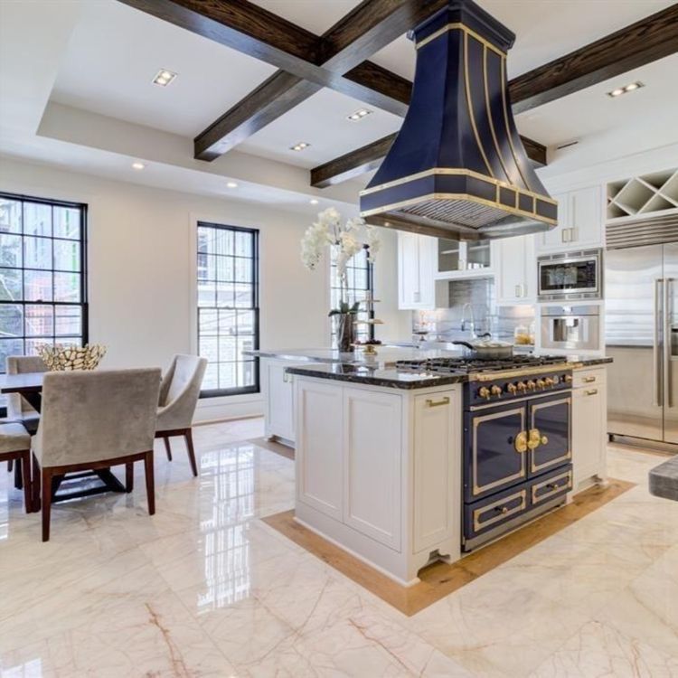 Bright modern kitchen with navy island range hood, white cabinets, marble floors, and adjacent dining area