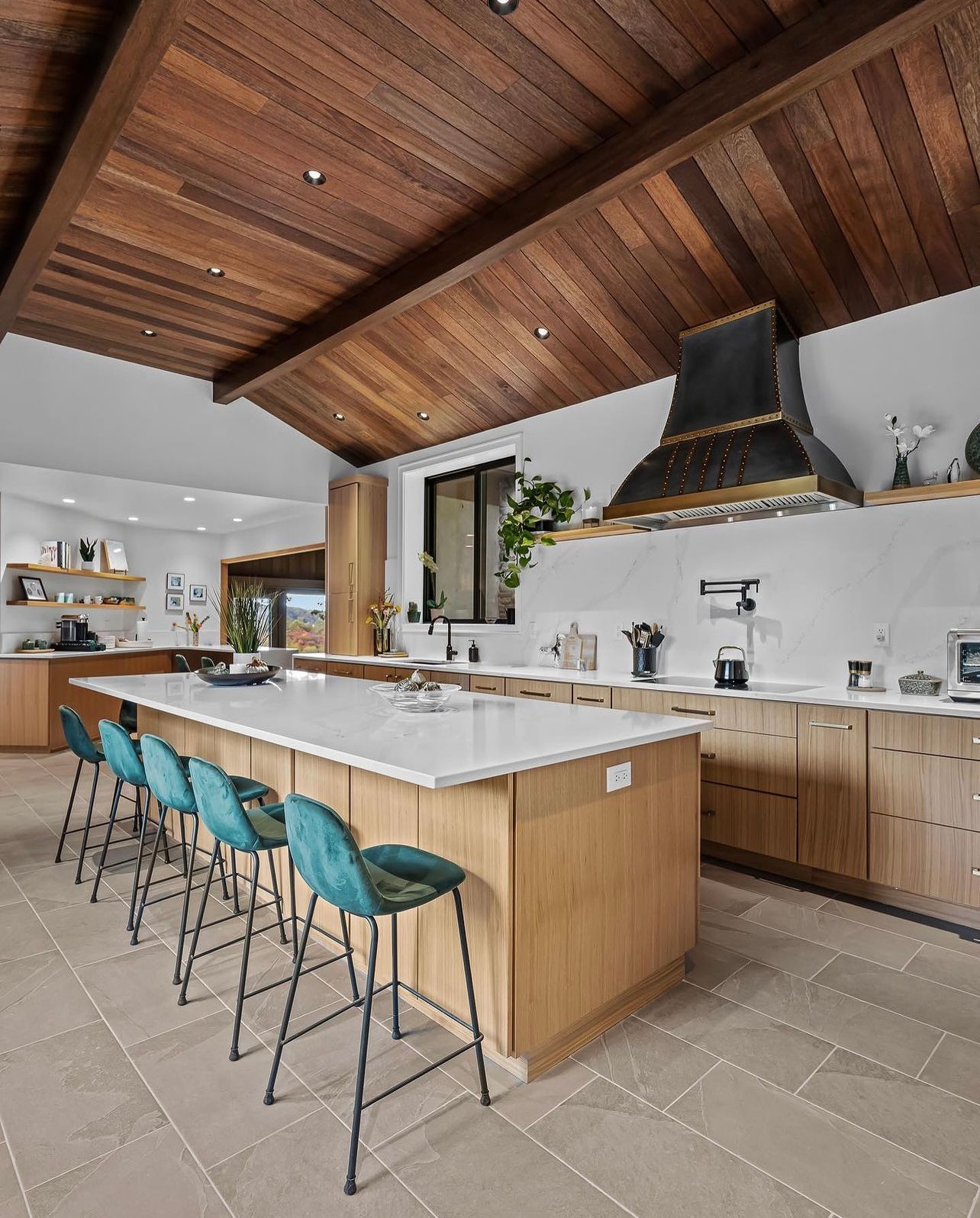Modern kitchen with wood ceiling, large island, teal bar stools, and black range hood