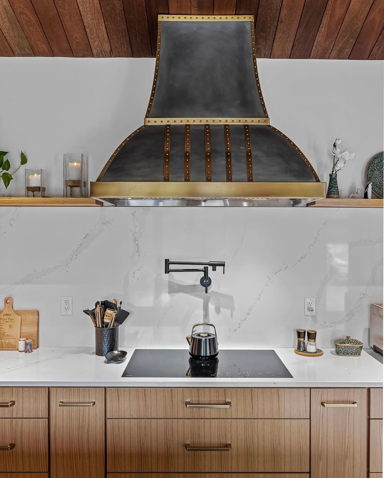 Modern kitchen with wood cabinets, marble backsplash, black range hood, and stovetop kettle