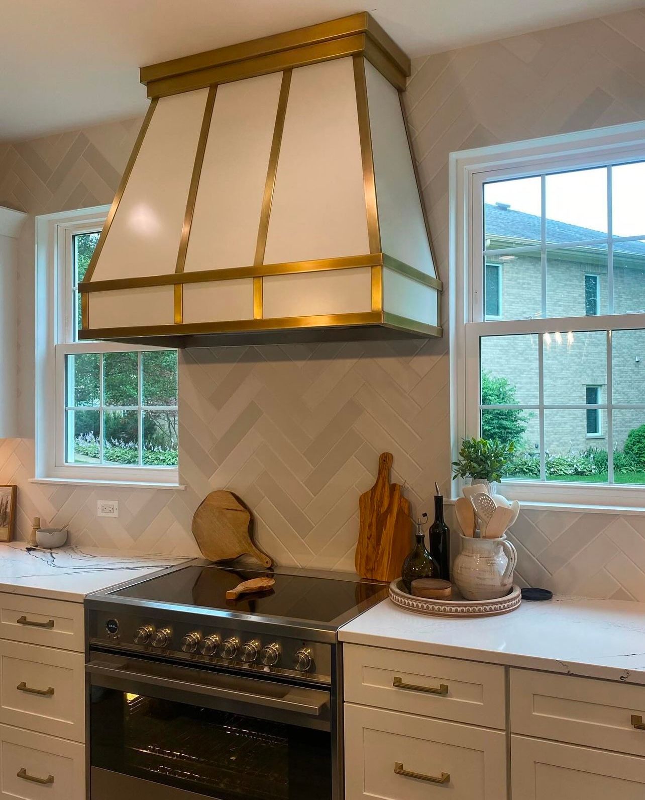 Bright kitchen with white cabinets, a stainless range, and a large gold-trimmed hood above the stove.