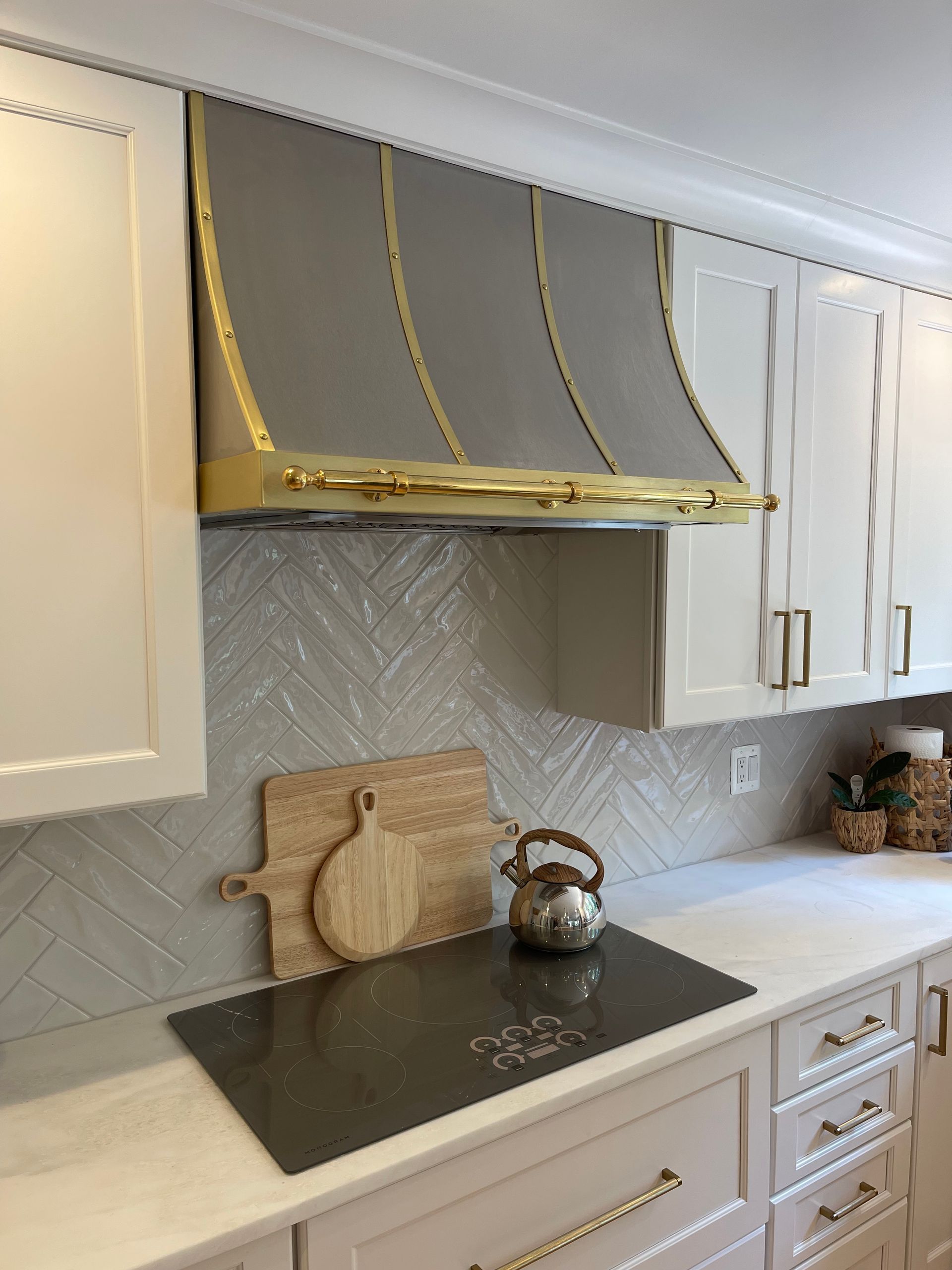 Modern kitchen with white cabinets, black countertop, gray backsplash, and gold-trimmed range hood