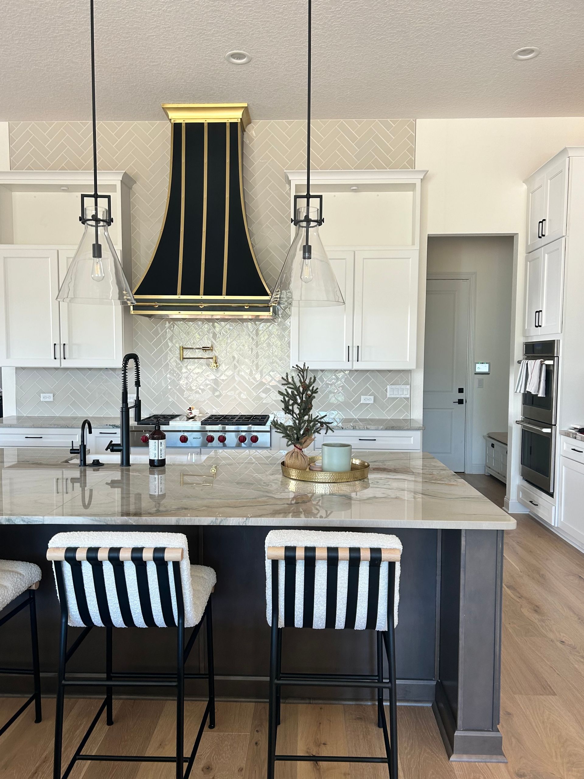 Modern kitchen with black island, striped stools, white cabinets, and gold-accent range hood