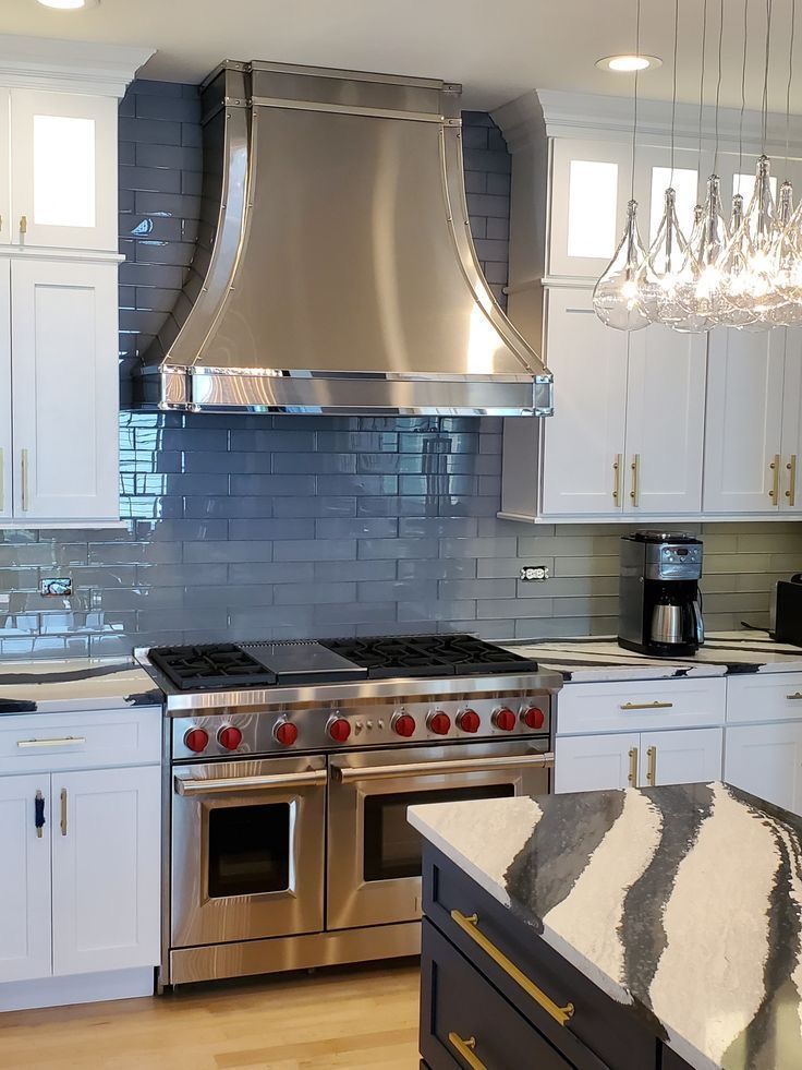 Modern kitchen with stainless steel range, blue tile backsplash, white cabinets, and a chandelier over an island