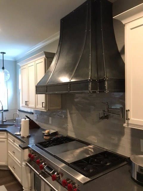 Modern kitchen with black range hood, white cabinets, and stainless steel stove and backsplash