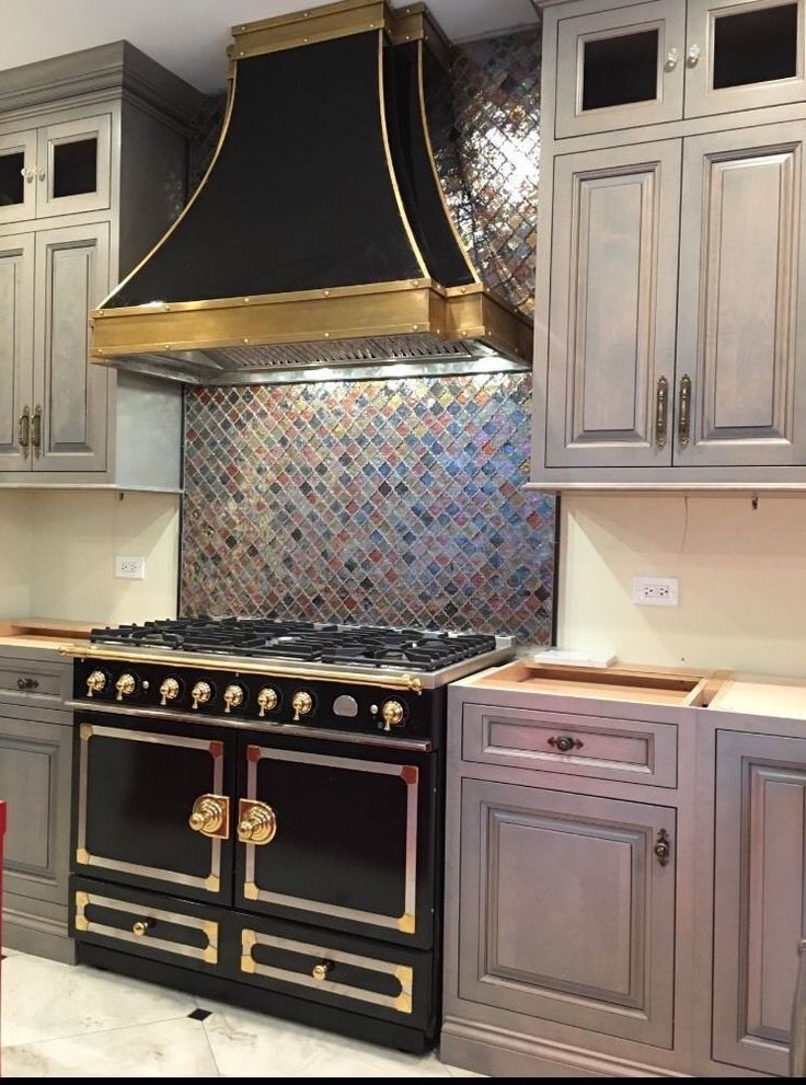 Black and gold stove and range hood between gray kitchen cabinets with mosaic tile backsplash