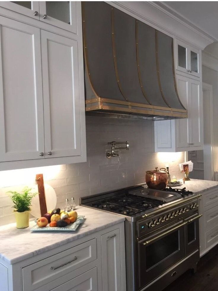 Modern white kitchen with marble counters, stainless range, and blue-gray vent hood.