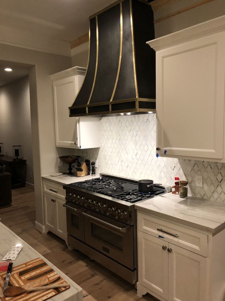 Elegant kitchen with black stove hood, stainless range, white cabinets, and marble backsplash