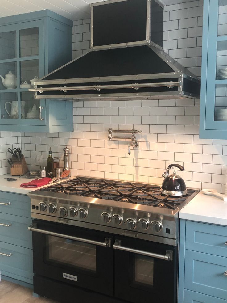 Blue kitchen with stainless steel range, black-and-white tile backsplash, and matching blue cabinets
