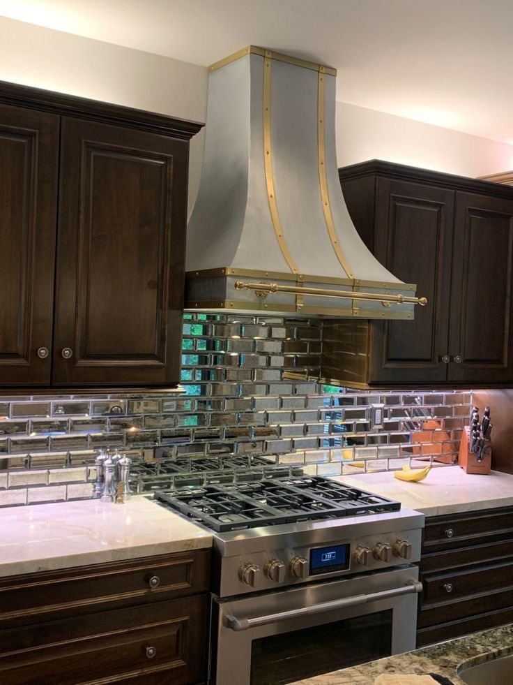 Modern kitchen with dark wood cabinets, stainless-steel range, and mirrored tile backsplash under a silver hood