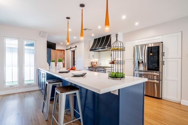 Bright modern kitchen with navy island, white countertops, pendant lights, and stainless steel appliances