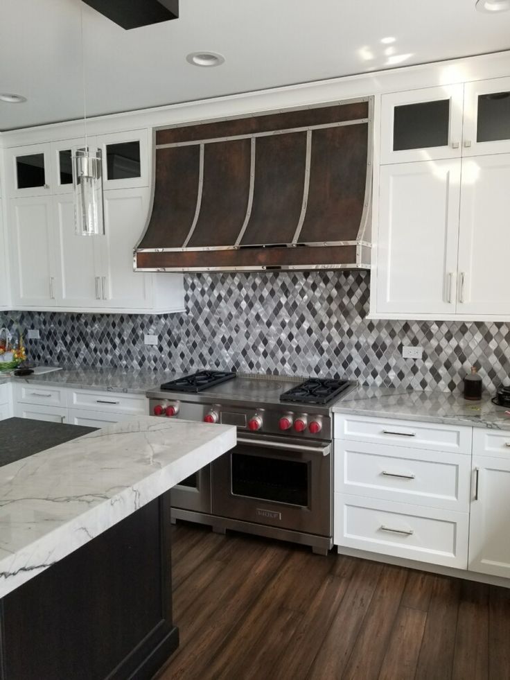 Modern kitchen with white cabinets, marble island, dark wood floor, and mosaic tile backsplash.