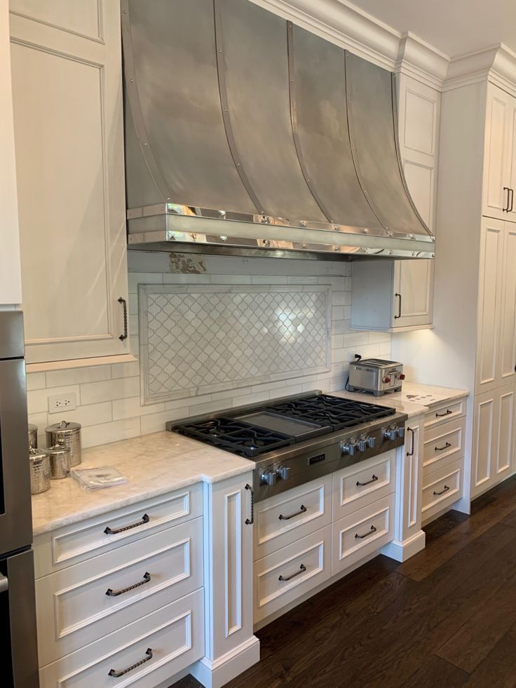 White kitchen with stainless steel range hood, gas stove, marble counters, and light wood floors