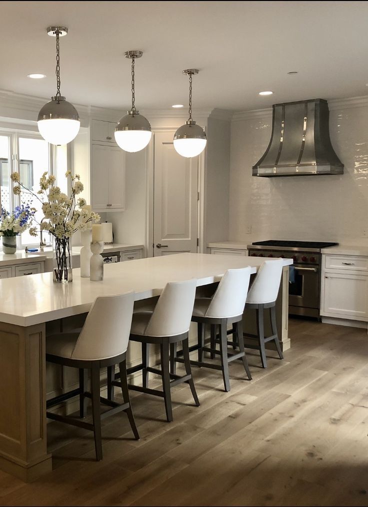 Modern kitchen with white island, pendant lights, bar stools, and stainless steel range hood