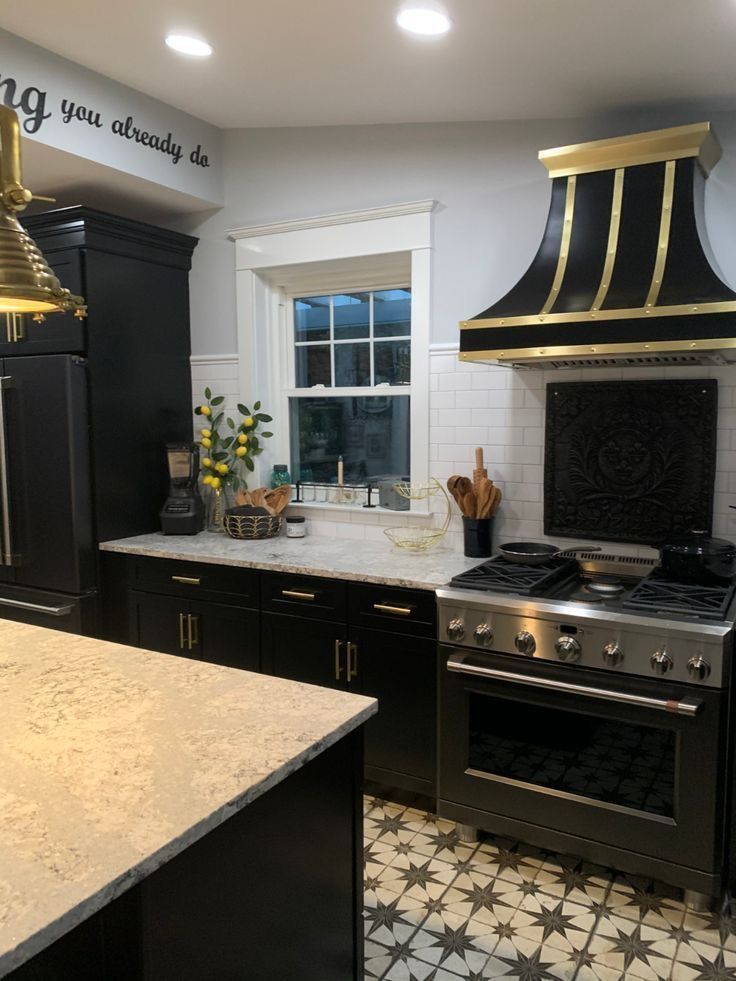 Modern kitchen with black cabinets, gold range hood, white tile, and patterned floor