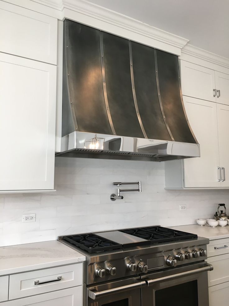 Modern kitchen with white cabinets, stainless steel range, and dark curved range hood