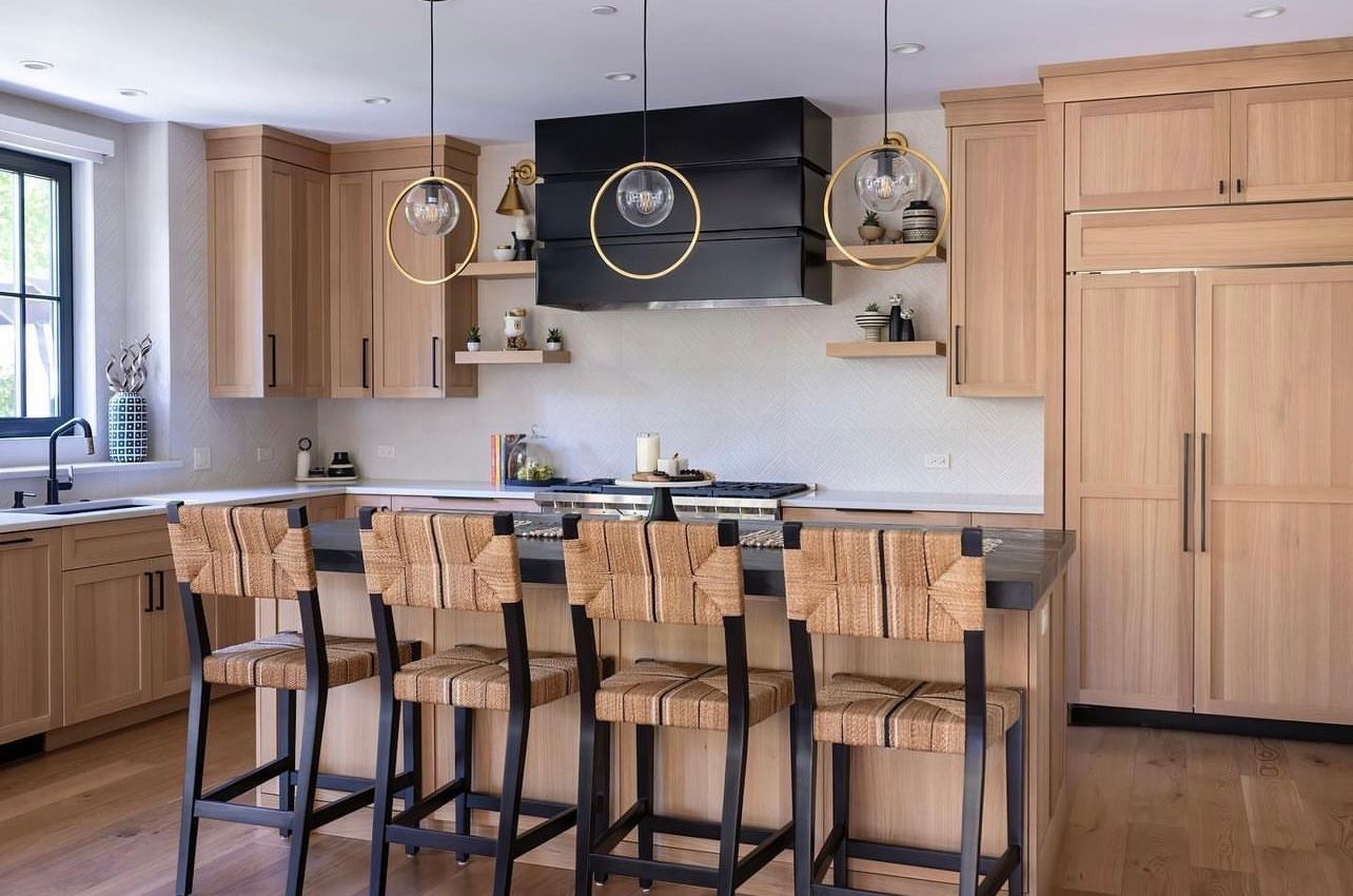 Modern kitchen with wood cabinets, island seating, pendant lights, and a large black range hood