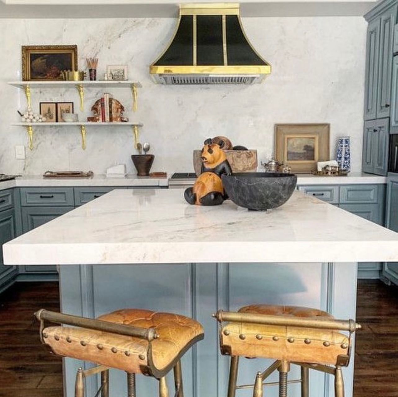 Modern kitchen with white island, blue cabinets, black range hood, and two wooden stools