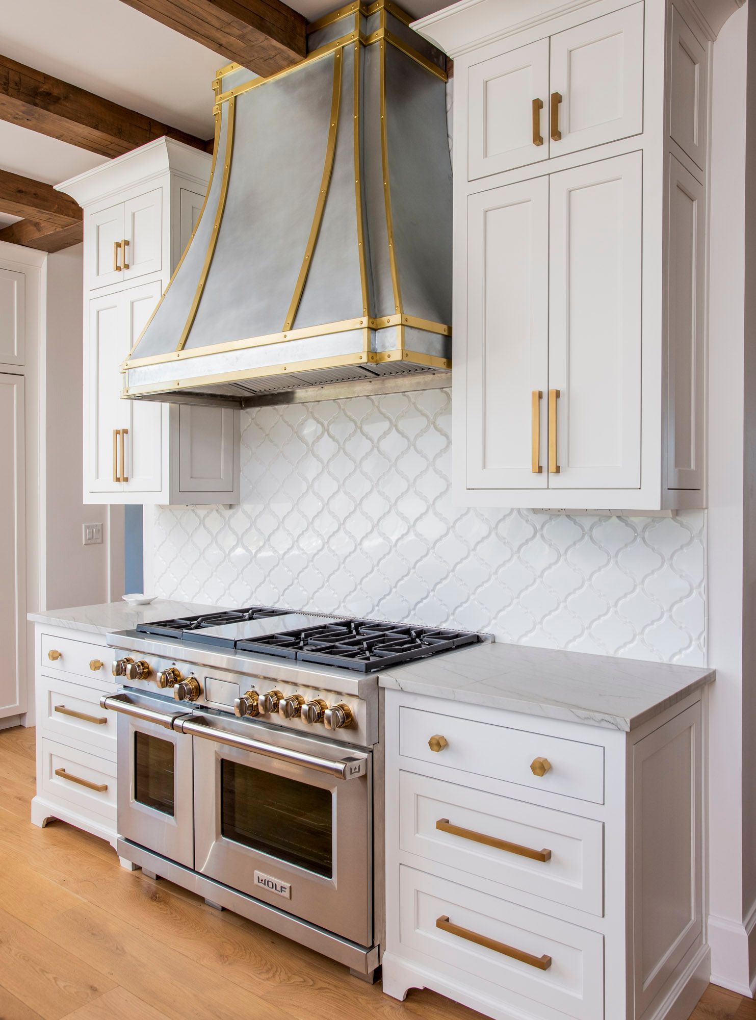 White kitchen with stainless range, marble-look backsplash, and gold-trimmed range hood