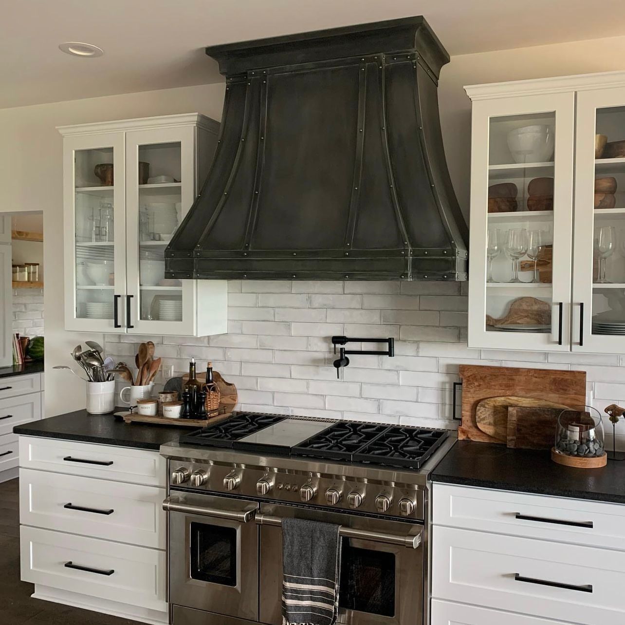 Modern white kitchen with black range hood, stainless stove, and white cabinets.