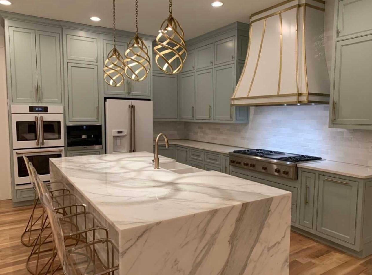 Modern kitchen with marble island, sage cabinets, pendant lights, and stainless steel appliances